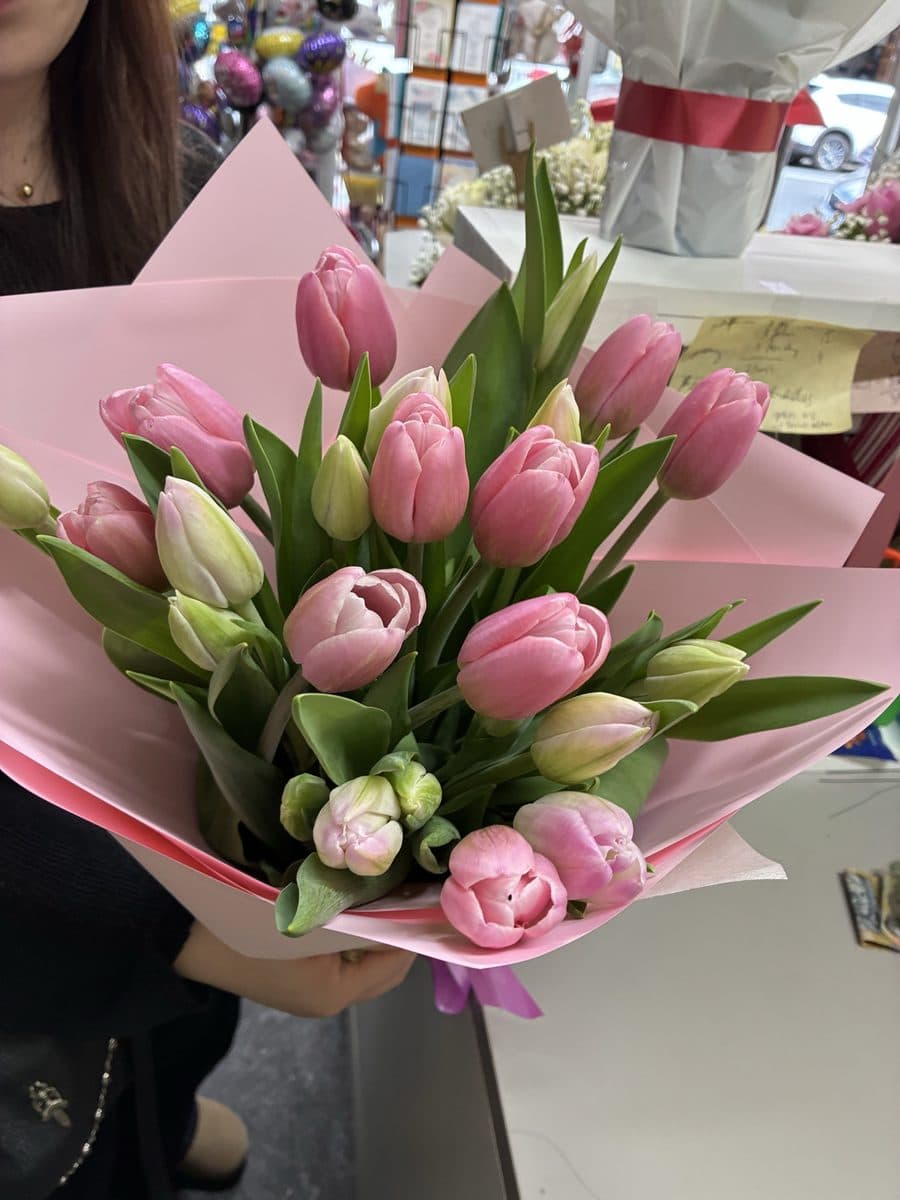 Bunch of pink and white tulips in blush pink wrap, held up in the shop