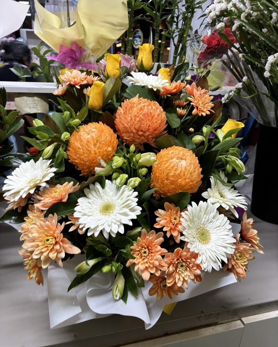 Box arrangement of orange chrysanthemums, white gerberas, yellow roses and peach daisies