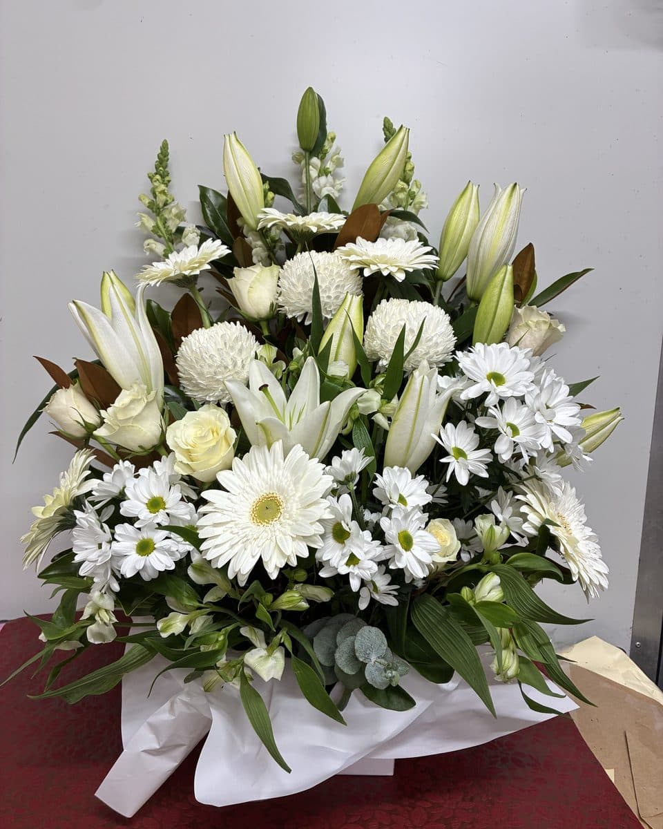 White arrangement of oriental lilies, chrysanthemums, gerberas and roses with magnolia leaves in a white box