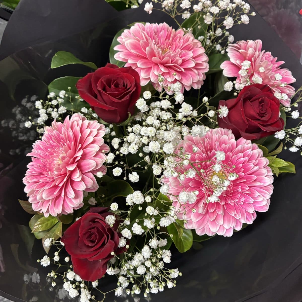 Pink gerberas, red roses and baby's breath in a black wrap, seen from above