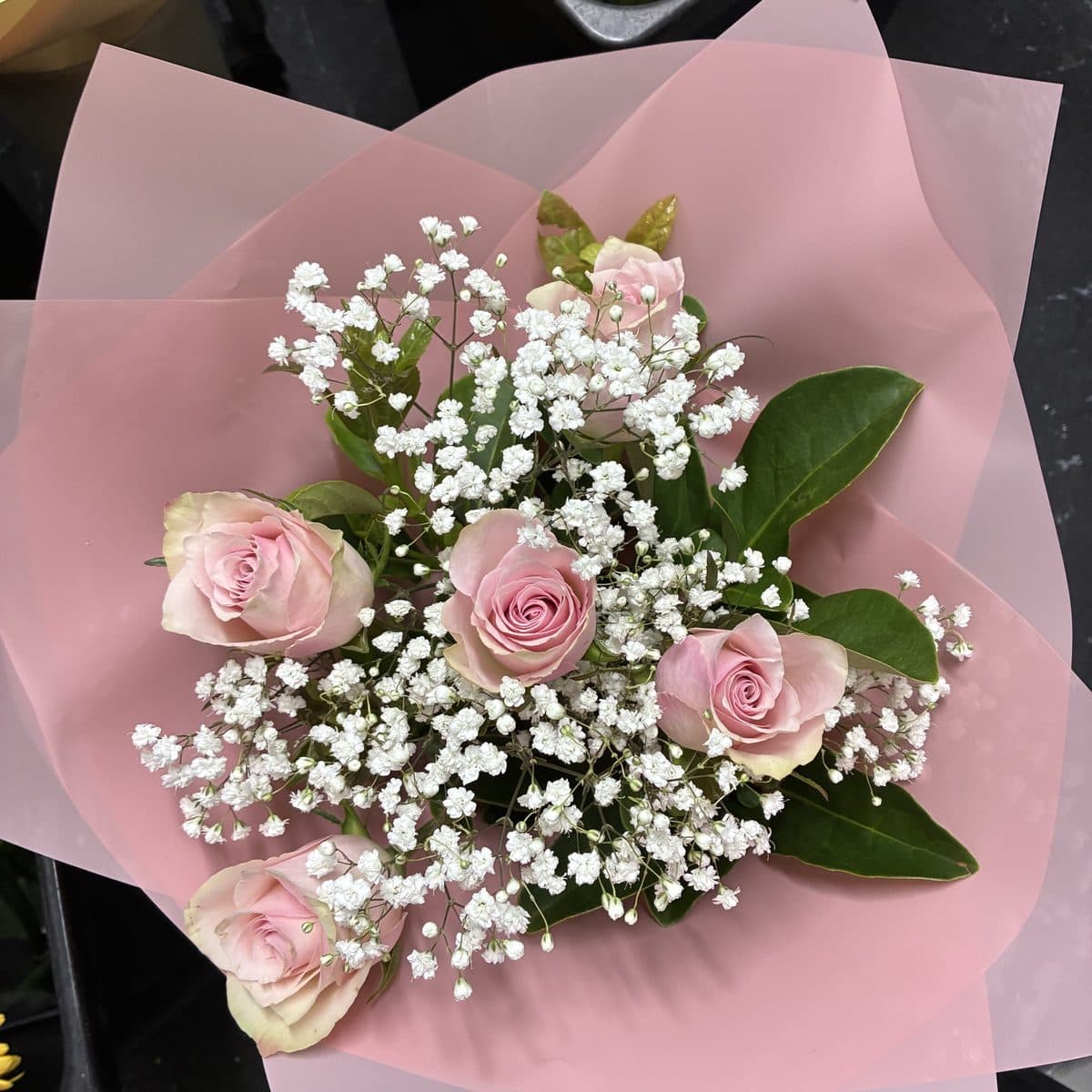 Soft pink roses with baby's breath in a pale pink wrap, seen from above