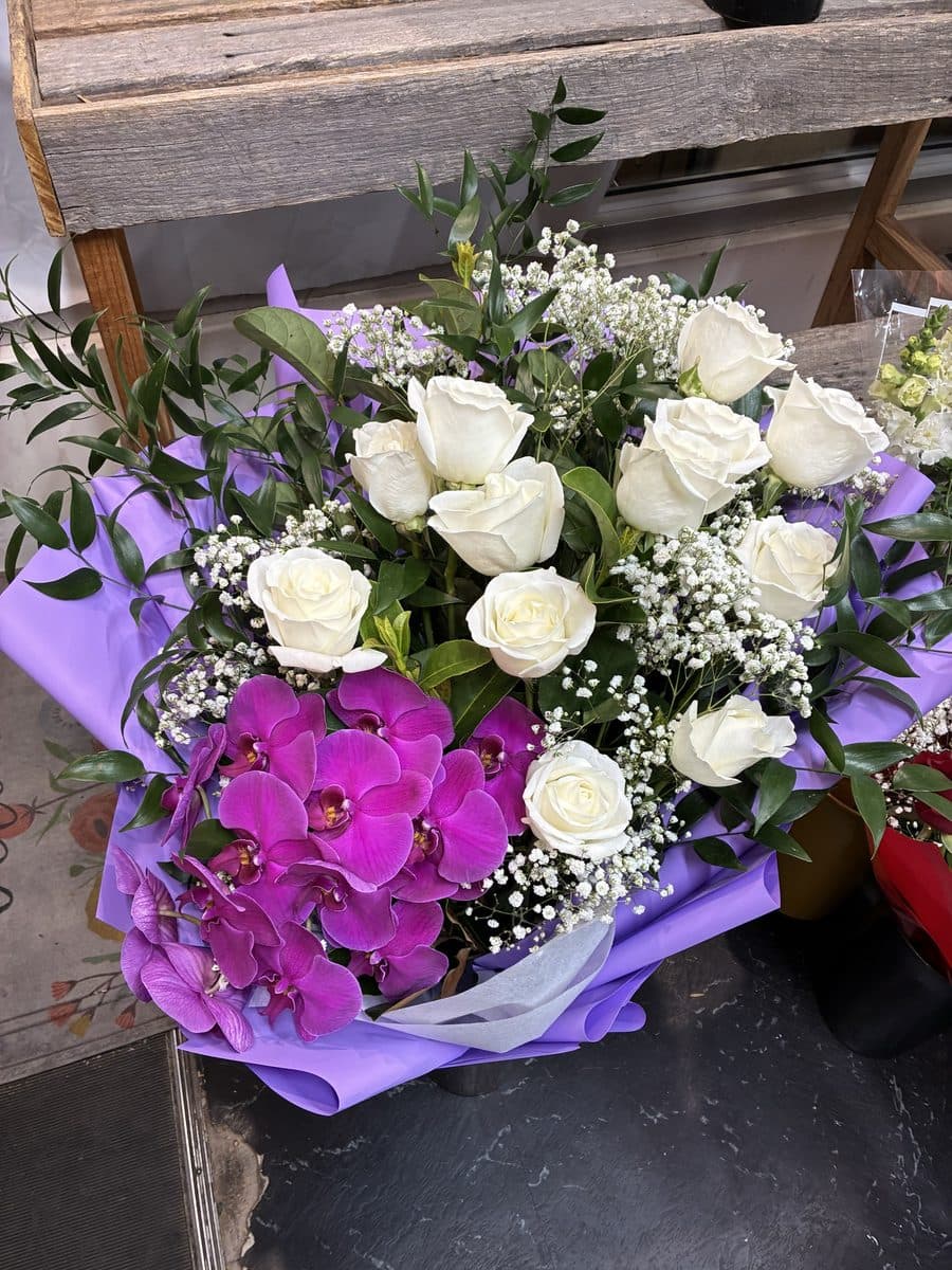 White roses and baby's breath with a stem of magenta phalaenopsis orchid, wrapped in lilac paper